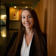 Alex, a white woman with brown hair, wears a white blouse and black blazer. 