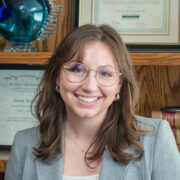 Amanda, a white woman with brown hair, wears a white blouse and grey suit.