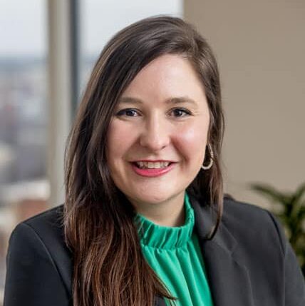 Melissa, a white woman with brown hair, wears a green blouse and black blazer.