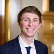 Brad, a white man with brown hair, wears a white shirt, black tie and black jacket.