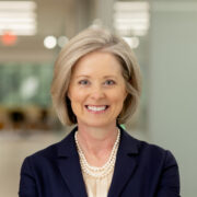 Christy, a white woman with blond hair, wears an ivory shirt and black jacket.