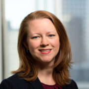 Christian, a white woman with red hair, wears a maroon blouse and black jacket.