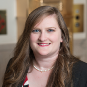 Jammie, a white woman with brown hair, wears a white and red dress and black jacket.