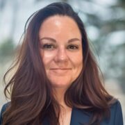 Kelly, a white woman with brown hair, wears a dark blue suit.