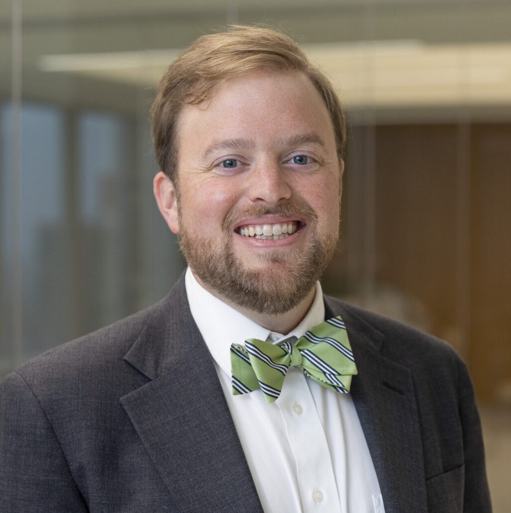 Otis Walker, a white man with light brown hair and a beard, wears a white shirt and green bowtie.