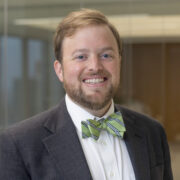Otis Walker, a white man with light brown hair and a beard, wears a white shirt and green bowtie. 