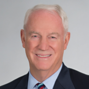 Richard, a white man with white hair, wears a pale blue shirt, striped tie and black jacket.
