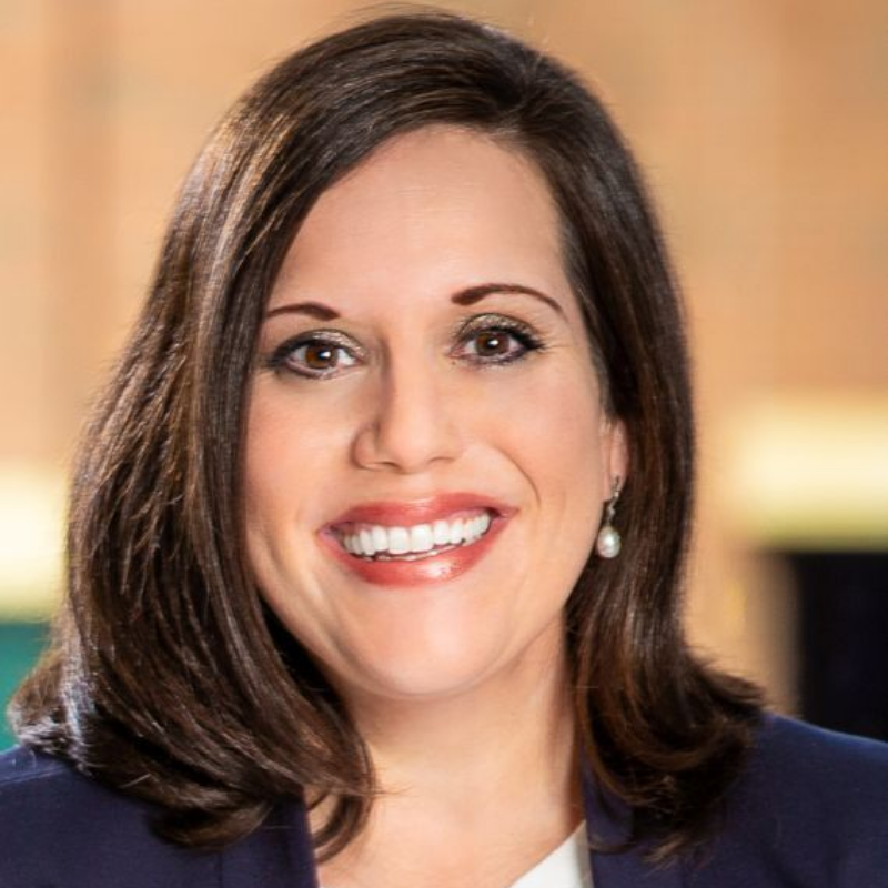 Amy, a white woman with brown hair, wears a white blouse and blue blazer.