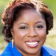 LJ, a Black woman with black hair, wears a blue button-down blouse and silver jewelry.