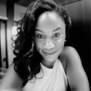 Quinn, a Black woman with curly black hair, wears a white blouse. 