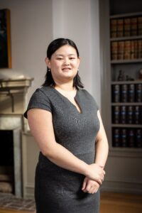 Melissa, a woman with dark brown hair, wears a black dress. She is smiling.