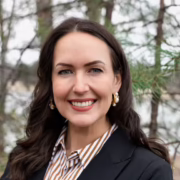 Mary, a white woman with brown hair, wears a brown and white button down blouse and a brown jacket.