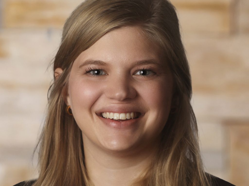 Christiana, a white woman with blond hair, wears a black blouse.