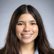 Isabella, a Hispanic/Latina woman with brown hair, wears a pale blue blouse and black suit. 