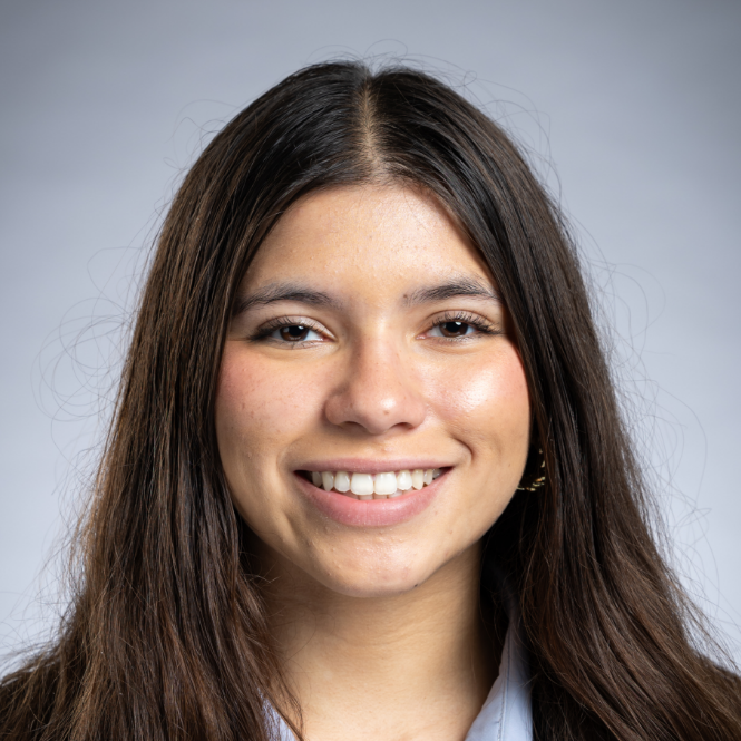 Isabella, a Hispanic/Latina woman with brown hair, wears a pale blue blouse and black suit.
