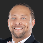 Joshua, a Black man with black hair, wears a white shirt and black suit. 