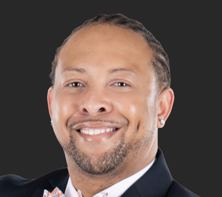 Joshua, a Black man with black hair, wears a white shirt and black suit.