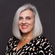 Nena, a white woman with grey hair, wears a black dress with white and beige print. 