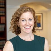 Claire, a white woman with curly blond hair, wears a green sleeveless dress. 
