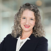 Diana, a white woman with grey hair, wears a white blouse and black jacket. 