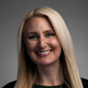 Alexandrea, a white woman with blond hair, wears a black dress and gold necklace.