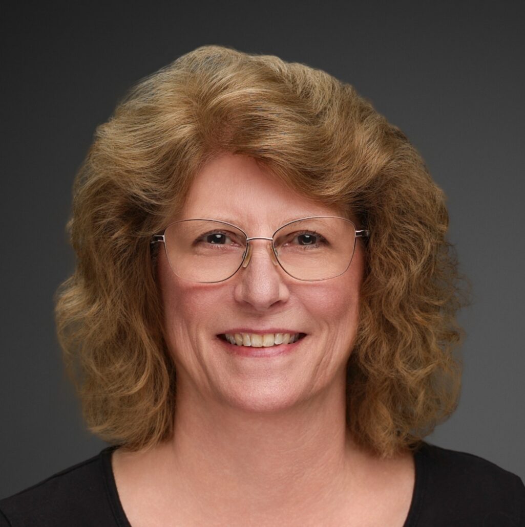 Peggy, a white woman with curly brown hair wears a black blouse.