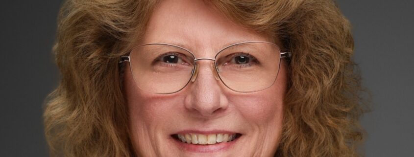 Peggy, a white woman with curly brown hair wears a black blouse.