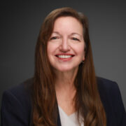 Annick, a whie woman with brown hair, wears a grey blouse and black blazer.