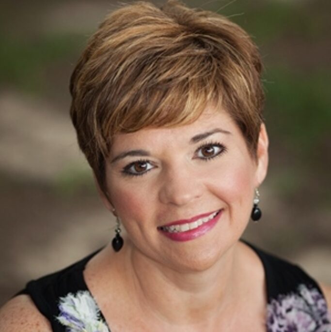 Sarah, a white woman with short auburn hair, wears a black shirt with white flowers.