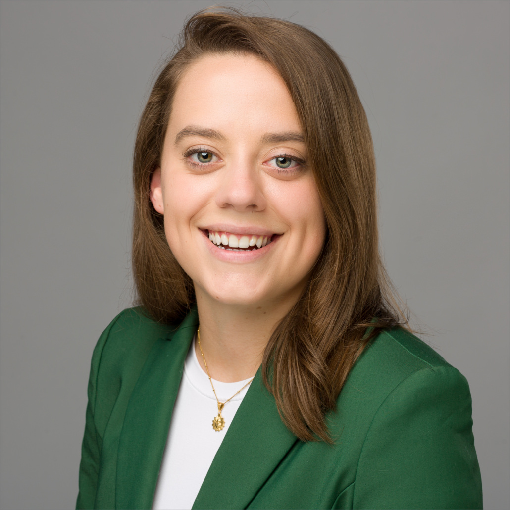 KimberMarie, a white woman with brown hair, wears a white shirt and green jacket and is smiling.