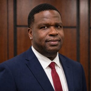 Tahje, a Black man with black hair, wears a white shirt, red tie and black suit.