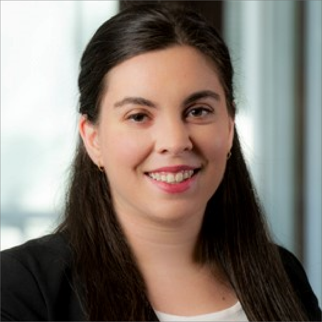 Sarah, a white woman with dark brown hair, wears a white shirt and black jacket.