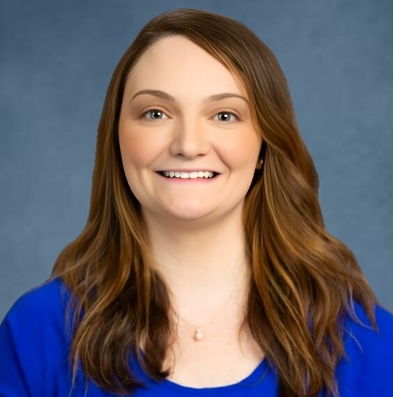Aimee, a white woman with brown hair, wears a royal blue blouse.