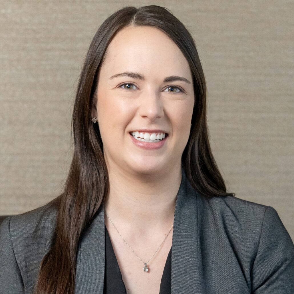 Andrea, a white woman with brown hair, wears a black blouse and grey blazer.