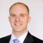 Daniel, a white man with brown hair, wears a white shirt, blue tie and black jacket.