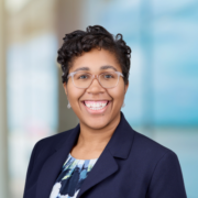 Taylor, a Black woman with black hair and glasses, wears a blue and white blouse and navy suit.