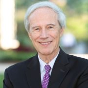 Dan, a white man with white hair, wears a white shirt, maroon tie and black jacket.