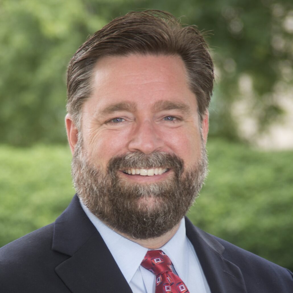 Steve, a white man with brown hair, wears a pale blue shirt, red tie, and black jacket.