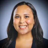 Jada, a woman with dark brown hair, wears a white blouse and suit.