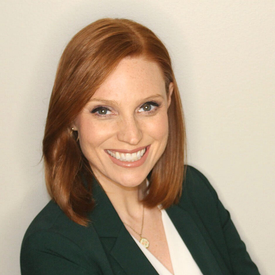 Janelle, a white woman with red hair, wears a white shirt and dark green jacket.