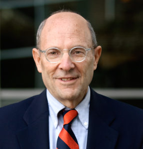 Jonathan, a white man with a shaved head and glasses, wears a blue shirt, blue and orange tie and navy suit.