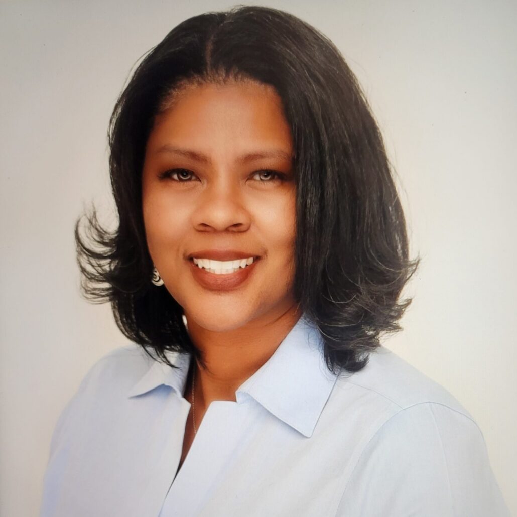 S.M. Kernodle-Hodges, a Black woman with brown hair and brown eyes, wears a blue button-down shirt.