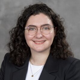 Christine, a white woman with curly black hair, wears a white shirt and black jacket.