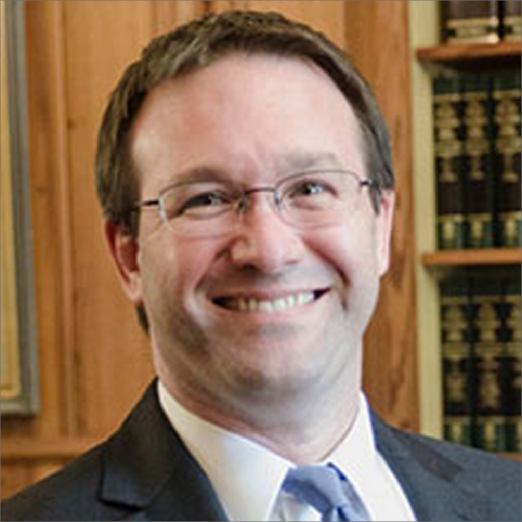 Bob, a white man with brown hair and wire glasses, wears a blue tie, white shirt, and black suit. He is smiling.