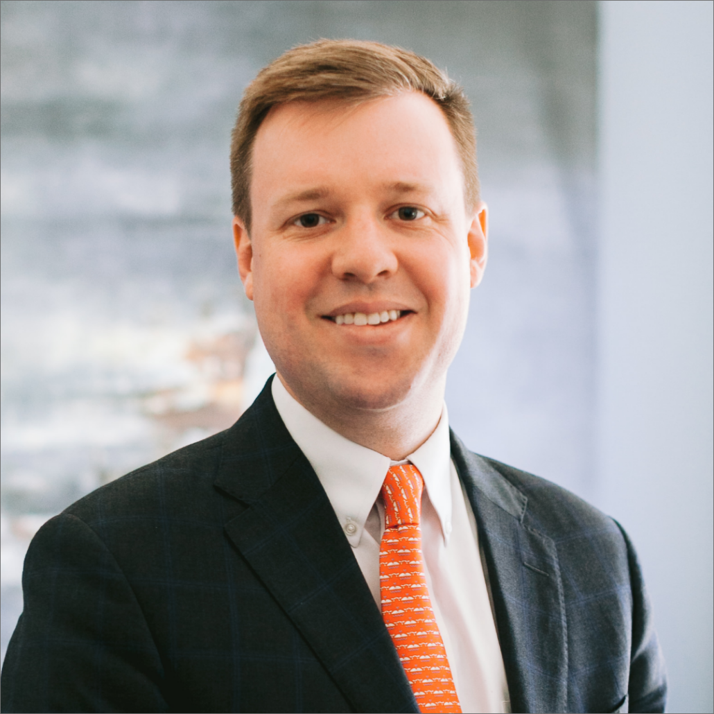 Carl, a white man with light brown hair, wears a white shirt, orange tie, and black jacket.