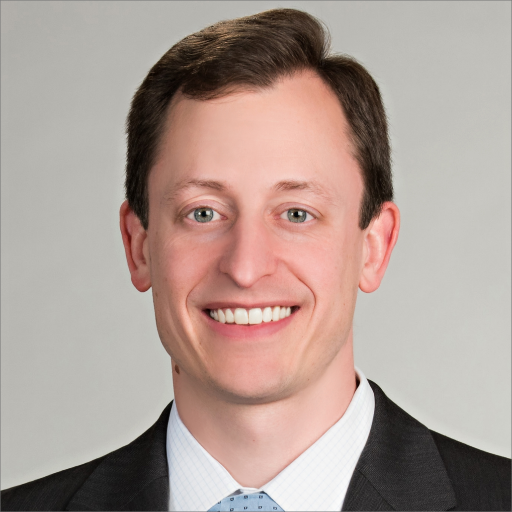 Greg, a white man with brown hair, wears a white shirt, blue tie and black jacket.