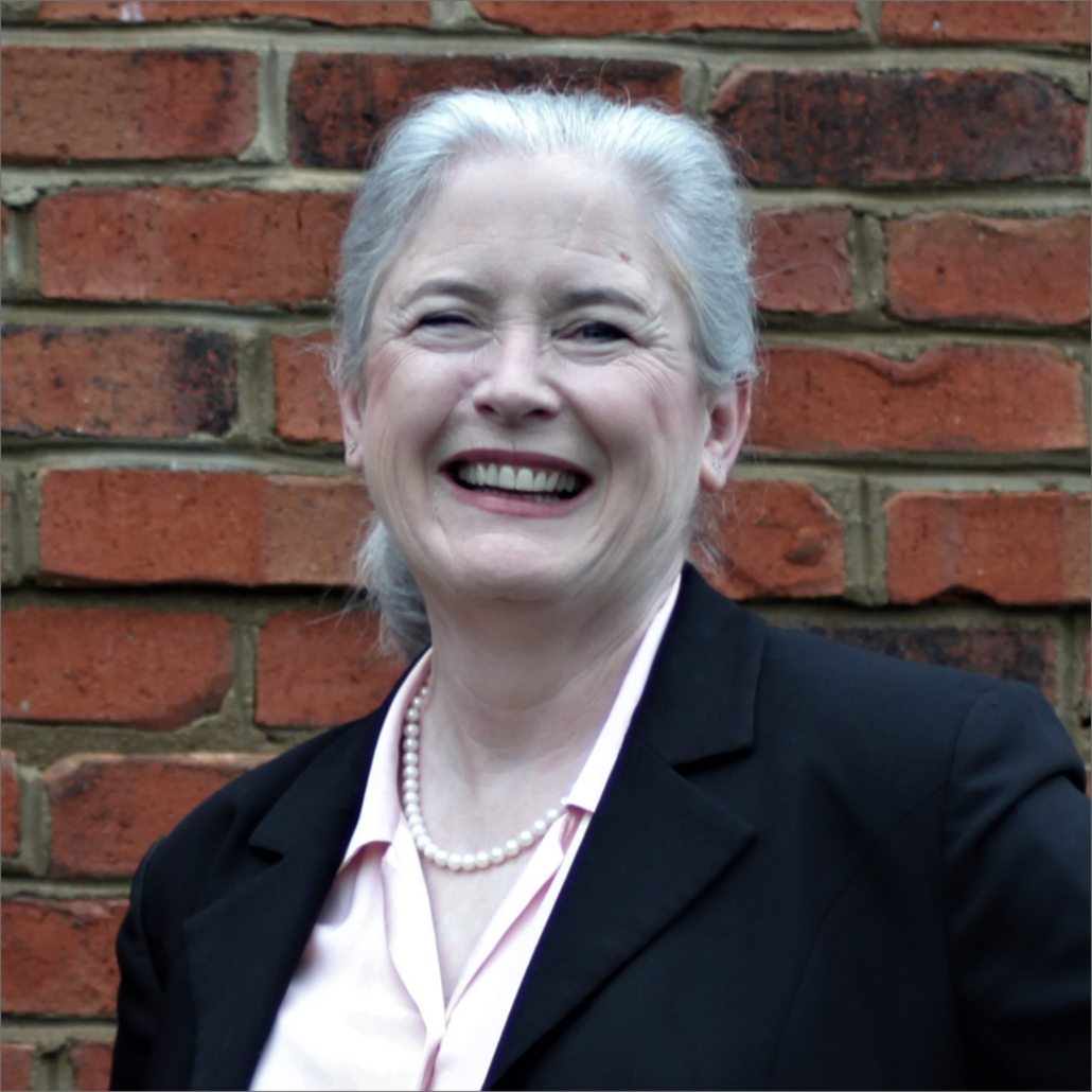 Jennifer, a white woman with white hair, wears a peach blouse, pearls, and a black blazer.