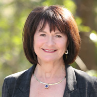 Judy, a white woman with brown hair, wears a black blouse and blazer and a silver necklace.