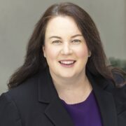 Rachel, a white woman with brown hair, wears a purple blouse and black blazer.