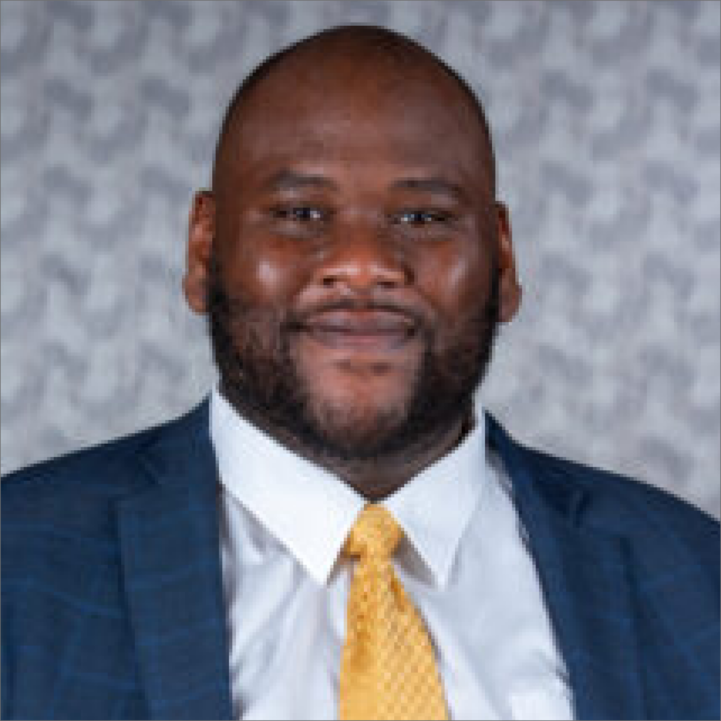 Salim, a Black man with black hair, wears a white shirt, yellow tie and navy jacket.